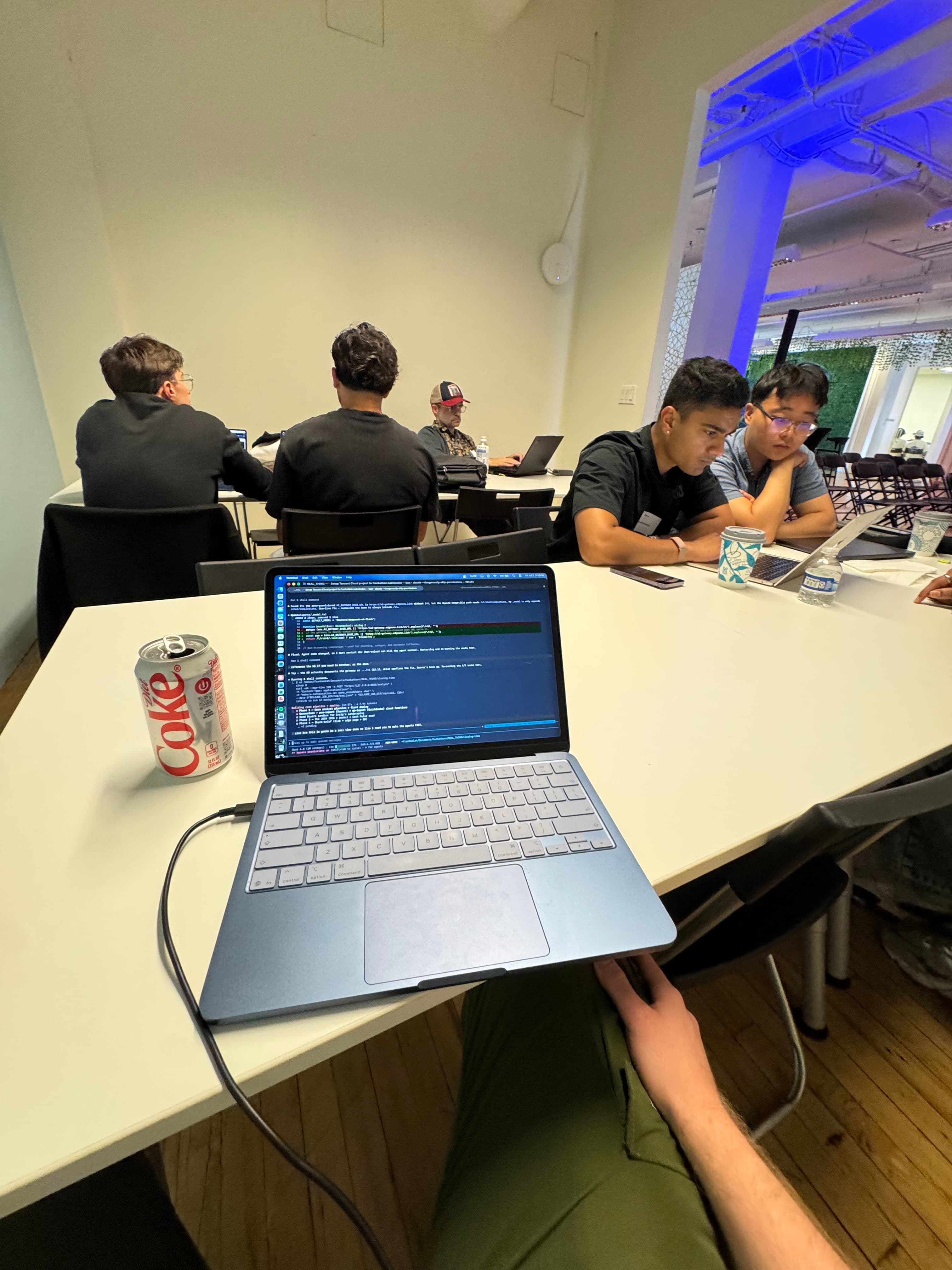 Laptop running multiple terminal agent sessions on a hackathon table, Diet Coke alongside