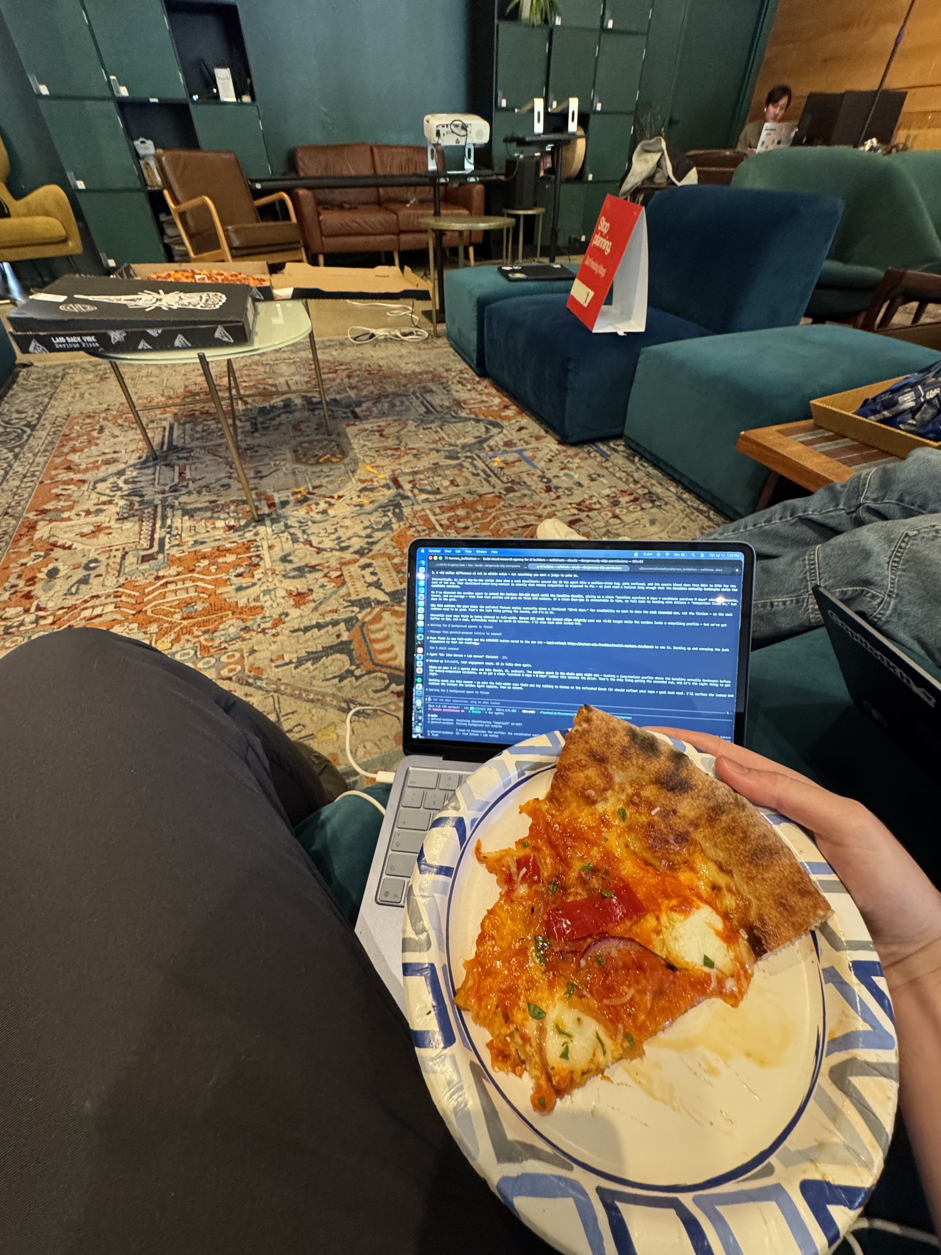 A slice of pizza beside a laptop running terminal experiments during the buildathon
